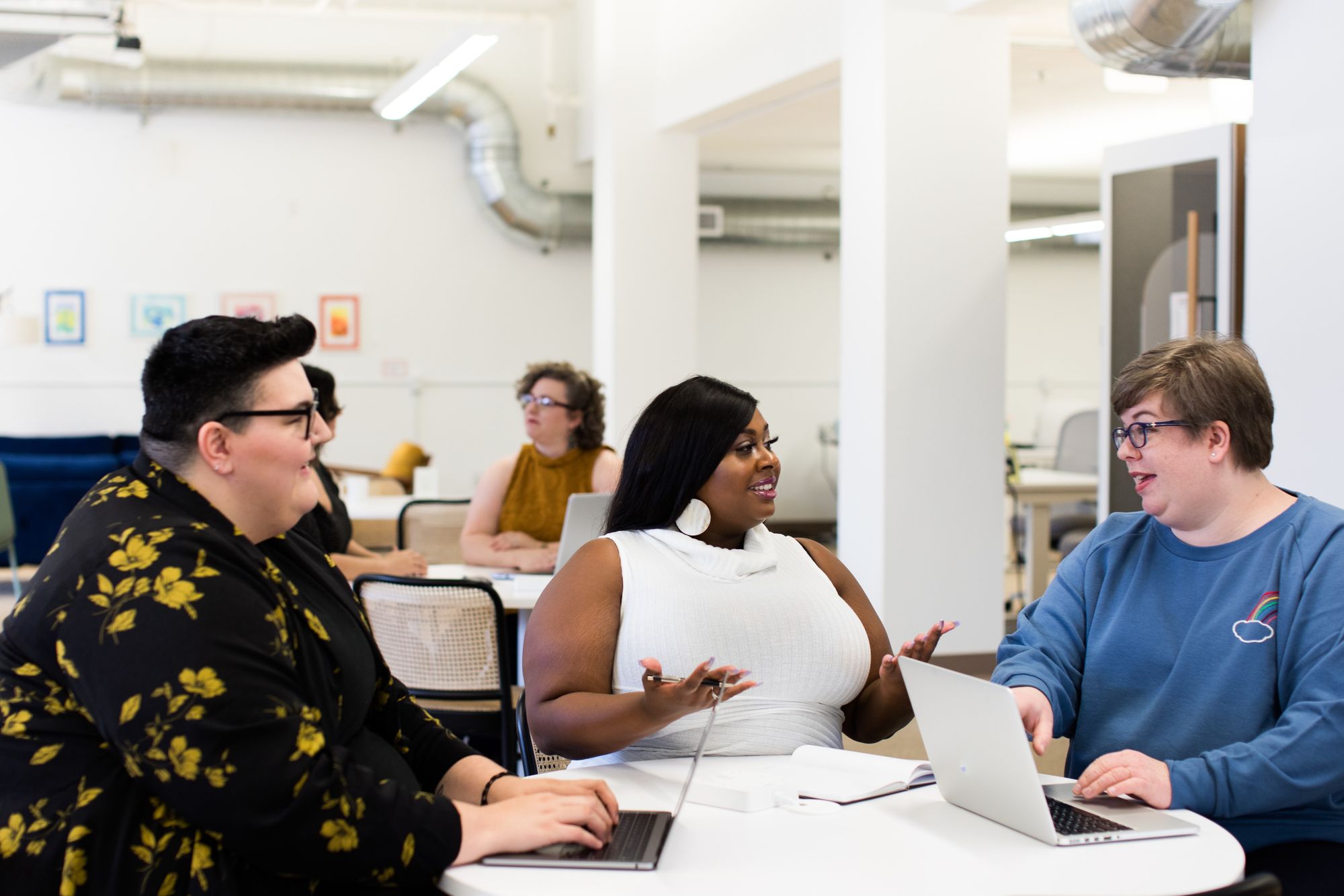 a group of three employees sit around a table in discussion.