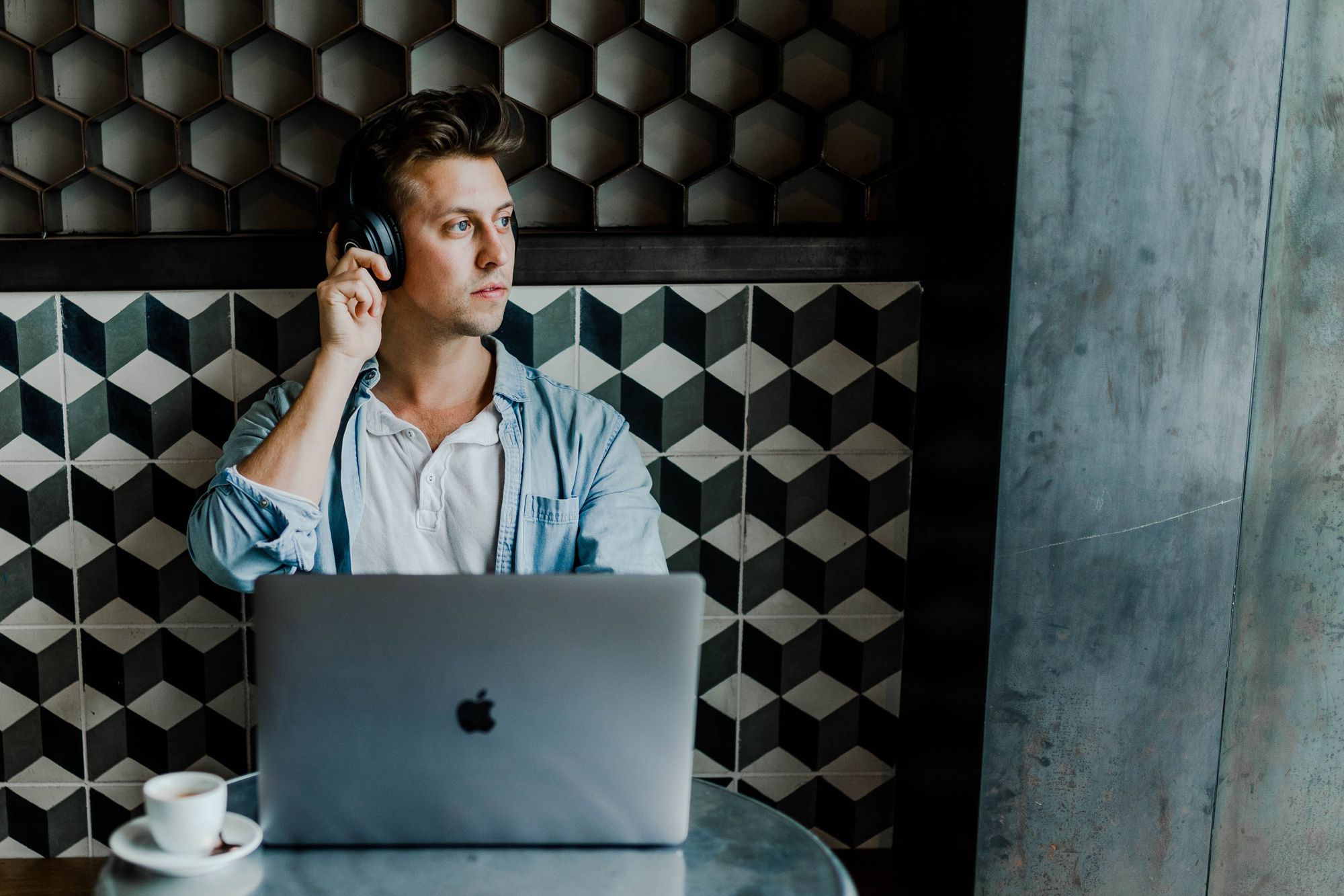 guy with headphones on in a café with a laptop and espresso in front of him.