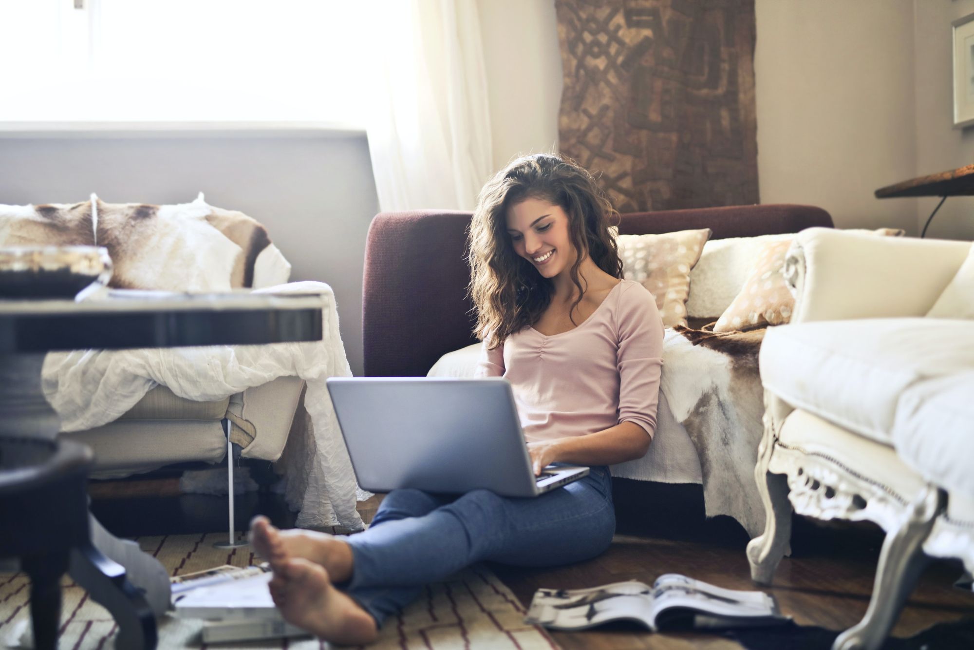 woman working remotely on a laptop sat on her living room floor and smiling.