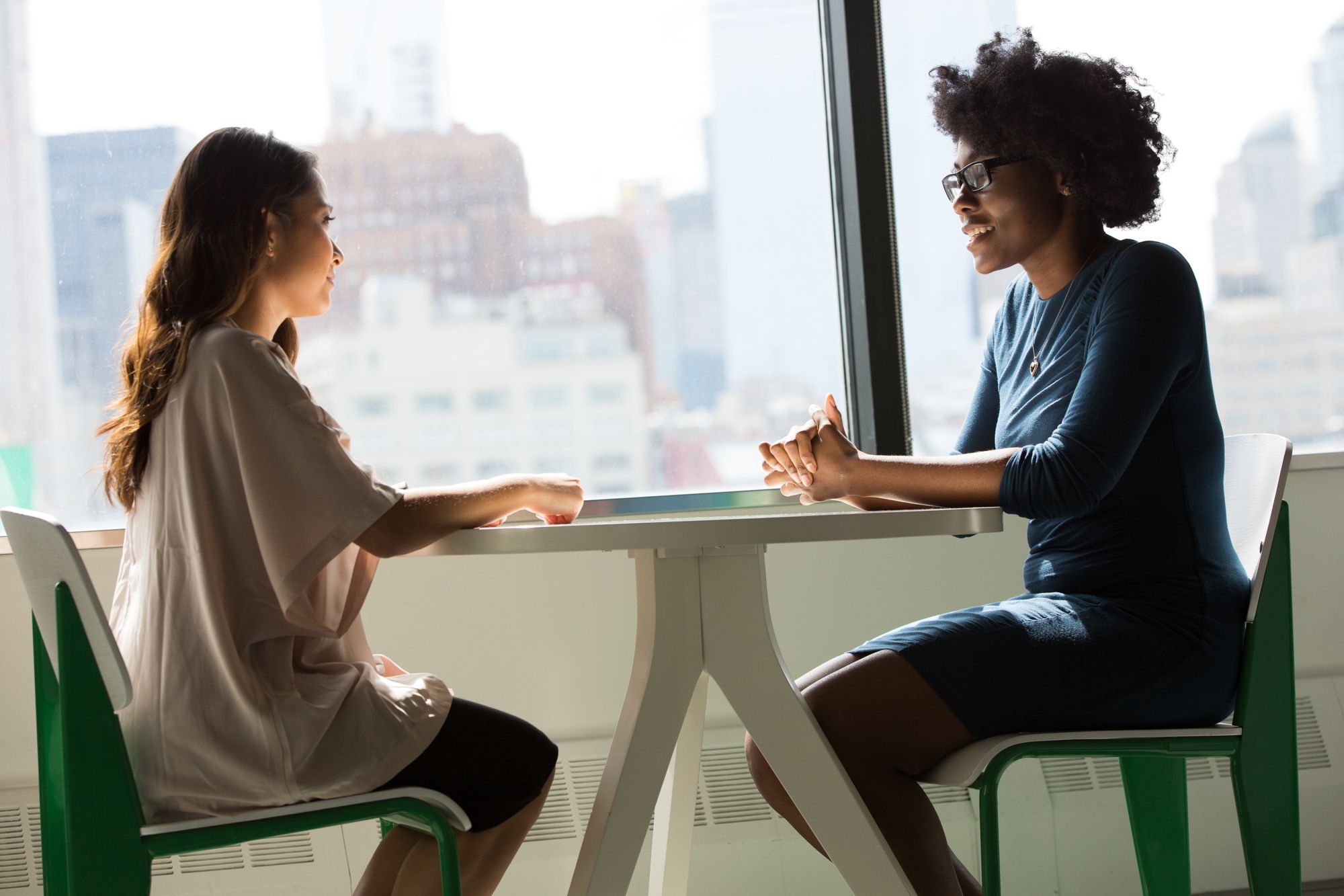 interview between two women sat opposite each other on a small table with a city skyline behind them.