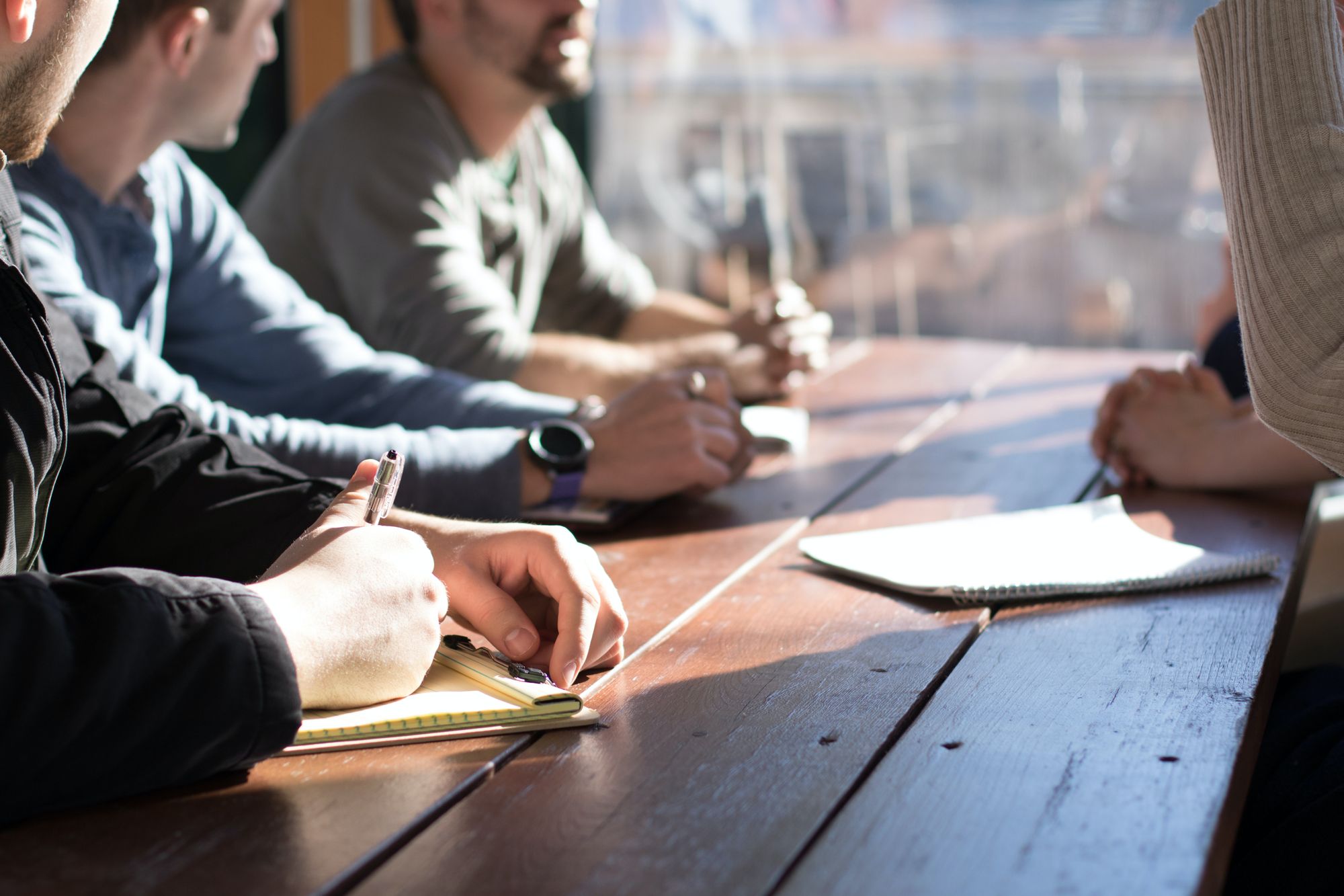 a group of people are sat along a bench, taking notes and talking