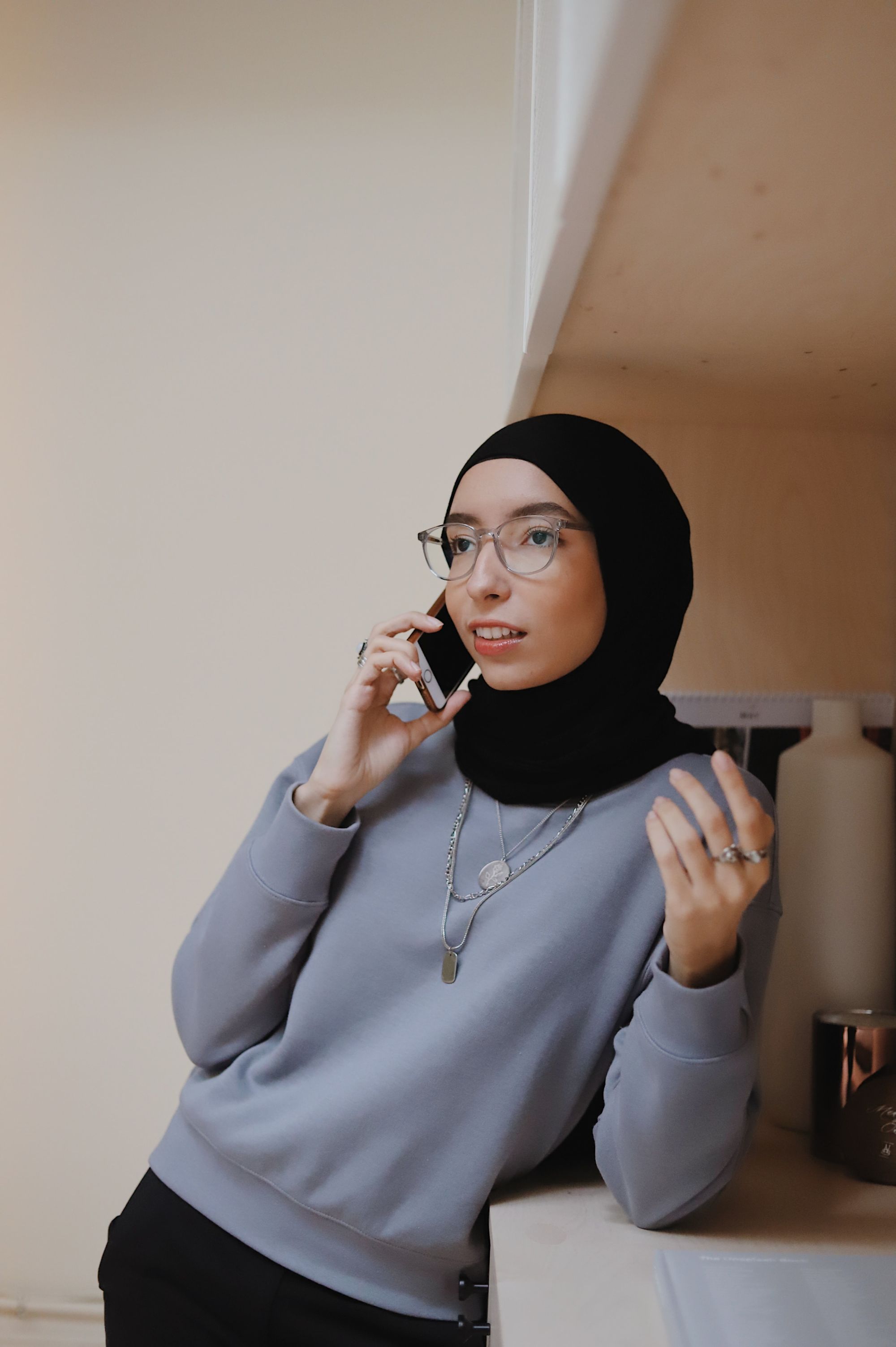 young woman with glasses and a headscarf is talking on the phone.