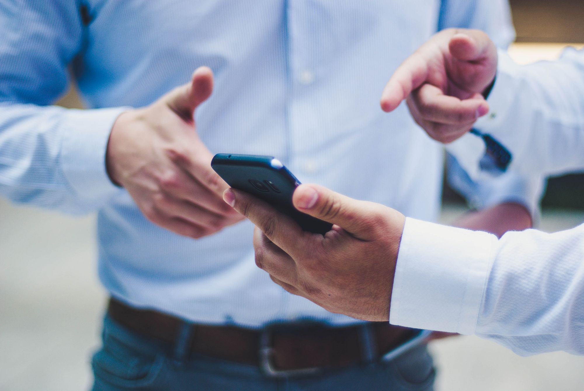 two men in suit shirts pointing at a smart phone in one of their hands