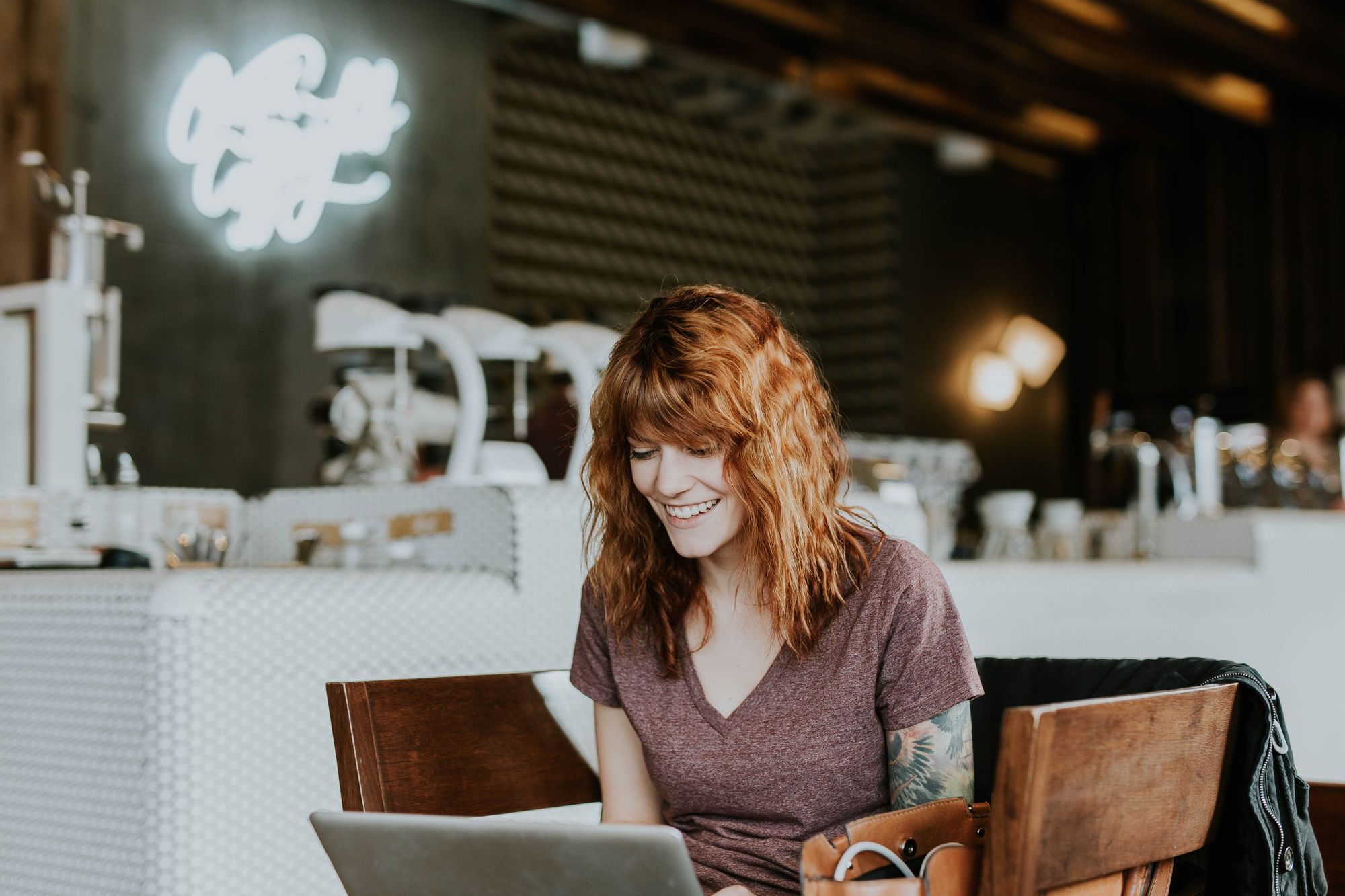 ginger haired employee with tattoo is looking at her laptop and smiling