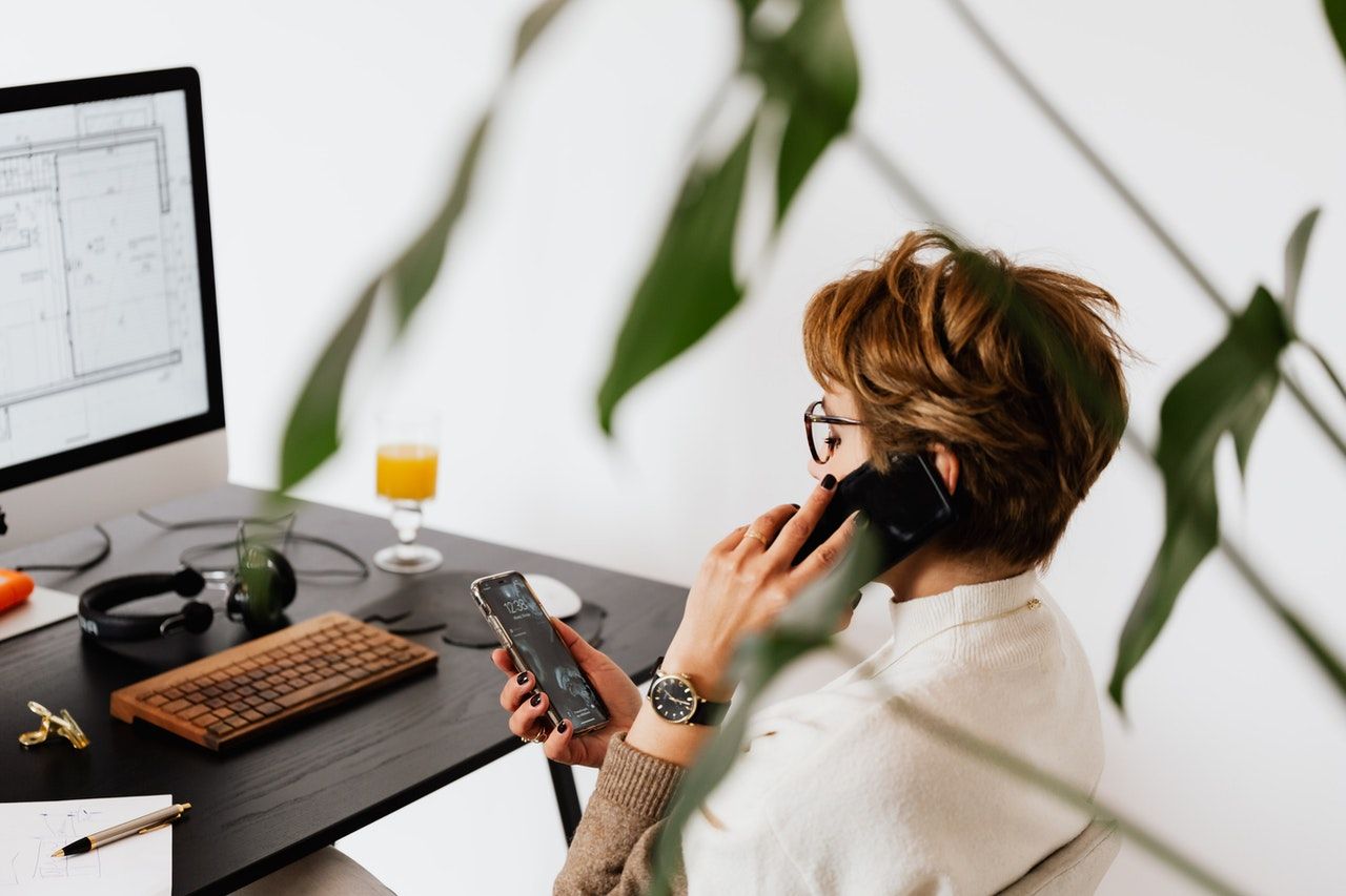 Female employee on the phone whilst looking at her smartphone in her hand.