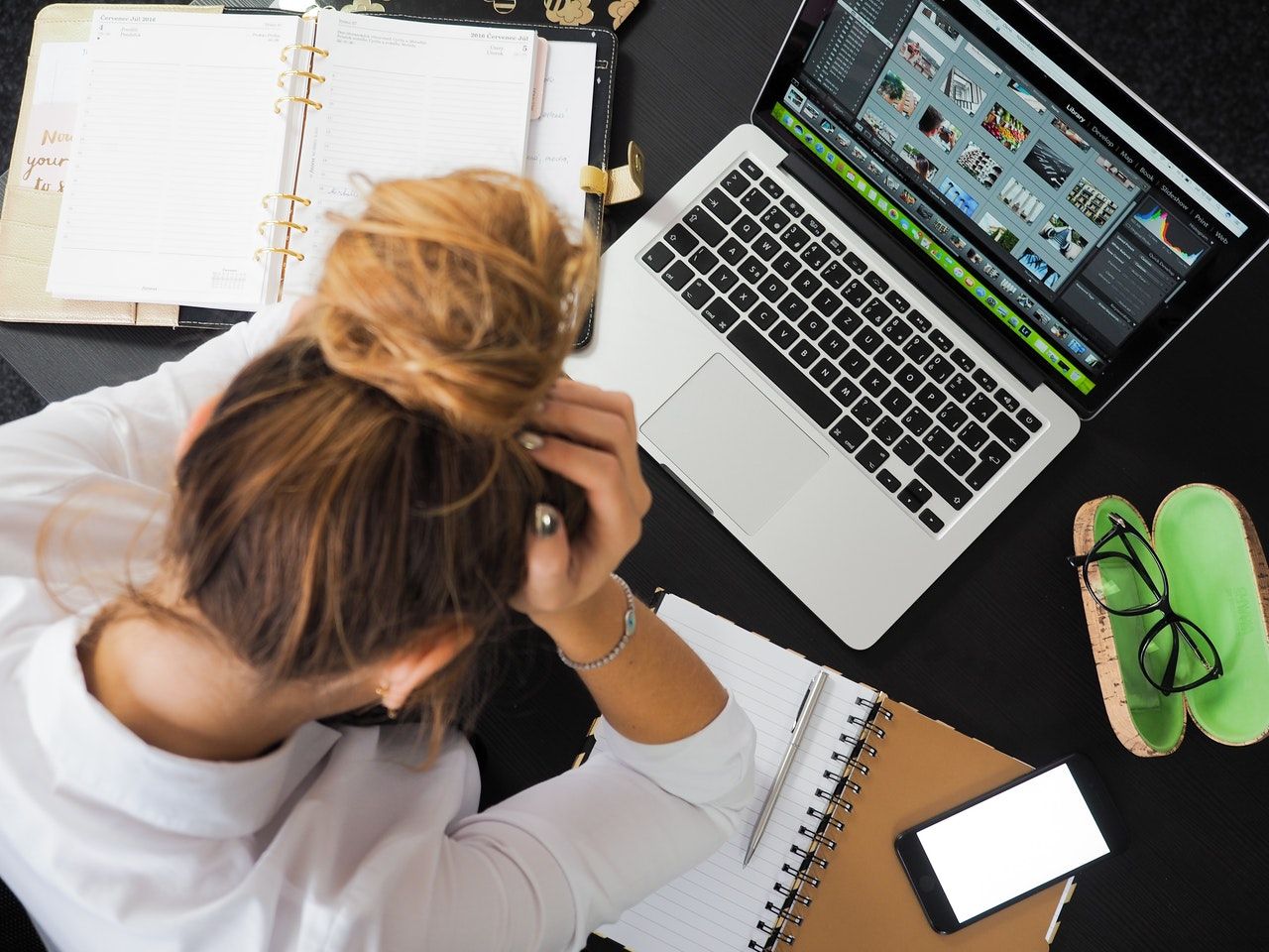 A lady sits a table with her laptop open holding her head in her hands.